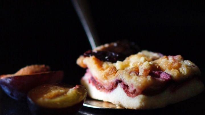 Ein Hefe-Obststreusel wird mit einer Portion auf einem L&ouml;ffel serviert, umgeben von frischen Pflaumenscheiben.