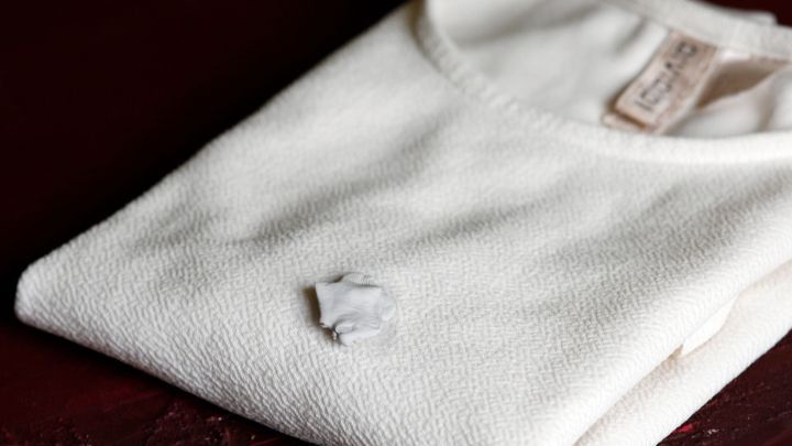 Ein wei&szlig;es Polyester-T-Shirt liegt ordentlich gefaltet auf einem Tisch, mit einem Kaugummi, der daran klebt.