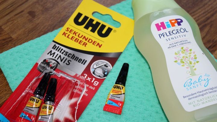 UHU Sekundenkleber und Baby&ouml;l liegen auf einer gr&uuml;nen Unterlage, bereit zum Entfernen von Kleber.