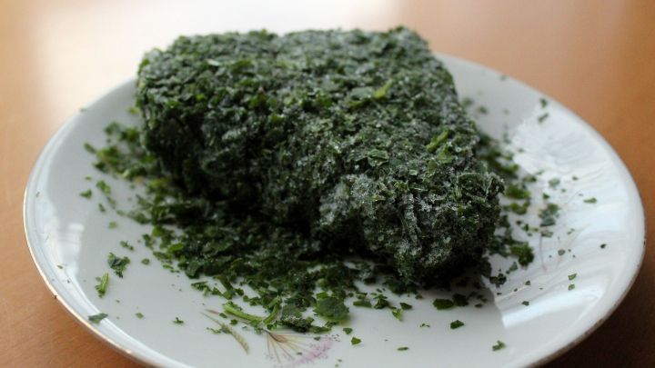 Ein Teller mit einer kr&auml;ftig gr&uuml;nen, gefrorenen Kr&auml;utermischung liegt auf einem Tisch. Die Kr&auml;uter bedecken eine Portion davon.