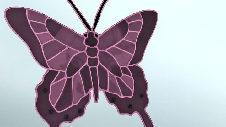 Ein lila Schmetterling aus farbigem Fensterfolie klebt an einer gl&auml;sernen Oberfl&auml;che und zeigt seine symmetrische Form.
