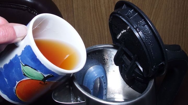 Eine bunte Tasse mit Fr&uuml;chtetee wird vorsichtig in einen Teekessel gegossen, um Kalkbildung zu vermeiden.