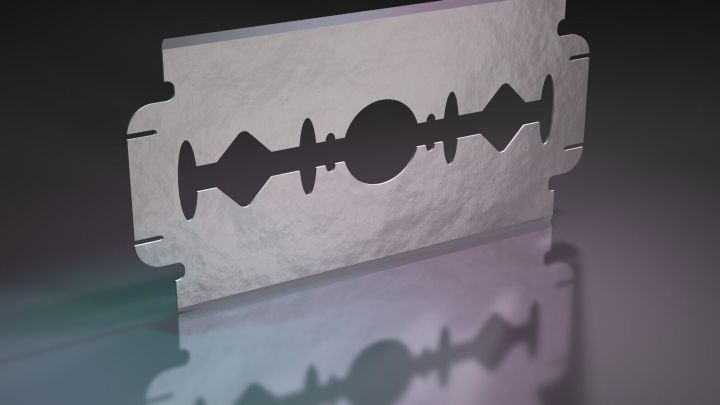 Eine Rasierklinge steht auf einer reflektierenden Oberfl&auml;che, bereit, um Fensterfarbe zu entfernen.