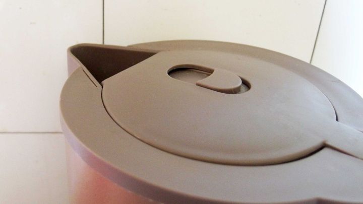 Ein K&auml;nnchen steht auf der K&uuml;che mit Fliesen, bereit, Fettflecken zu entfernen. Der Deckel zeigt eine praktische &Ouml;ffnung.