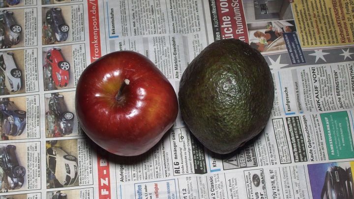 Ein roter Apfel und ein unreifer Avocado liegen nebeneinander auf einer Zeitungsseite zum schnellen Reifen lassen.
