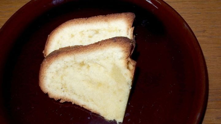 Zwei St&uuml;cke lockerer R&uuml;hrkuchen mit Buttermilch liegen auf einem braunen Teller, umgeben von einer einfachen Holzoberfl&auml;che.