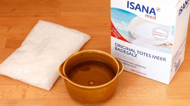 Ein Beh&auml;lter mit Wasser steht neben einem P&auml;ckchen Totesmeer Salz und einer Schachtel, bereit zur Anwendung gegen Pickel.