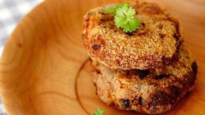 Zwei goldbraun gebratene Frikadellen liegen auf einem Holzbrett, garniert mit frischem Koriander, in einer appetitlichen Umgebung.