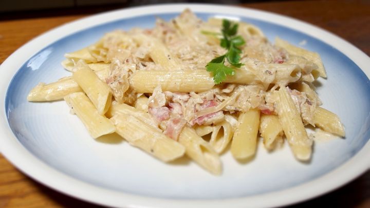 Eine appetitliche Nudelpfanne aus Penne, Sauerkraut und einer cremigen Sauce, angerichtet auf einem hellblauen Teller.