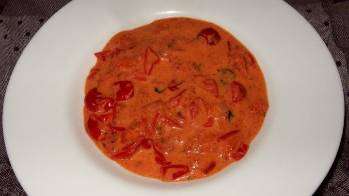 Eine cremige Tomatensuppe mit roten Tomatenst&uuml;cken liegt in einer wei&szlig;en Schale und l&auml;dt zum Probieren ein.