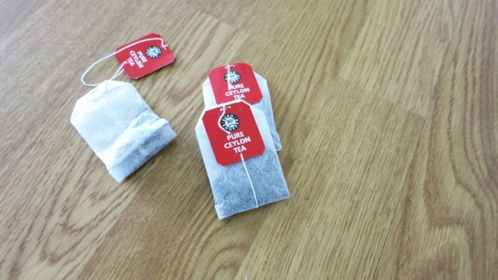 Drei Teebeutel liegen auf einem Laminatboden, umgeben von einem schlichten, hellen Holzdesign.