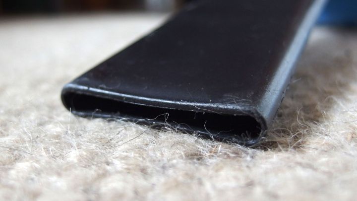 Ein schwarzes Staubsaugerrohr wird auf einem Teppich mit Tierhaaren positioniert, um diese aufzunehmen.