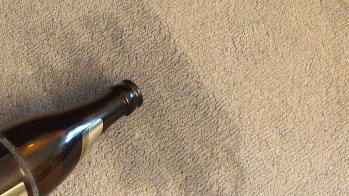 Eine Bierflasche liegt auf einem Teppich, hinterl&auml;sst einen Fleck, umgeben von einem neutralen Wohnraum.