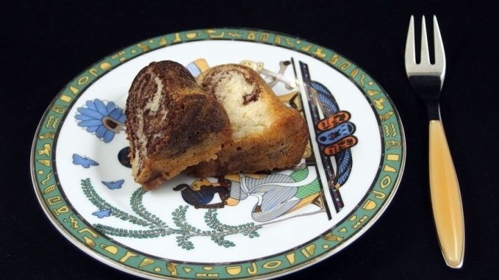 Ein St&uuml;ck Marmorkuchen mit Erdnussbutter liegt auf einem bunten Teller neben einer Gabel, vor schwarzem Hintergrund.