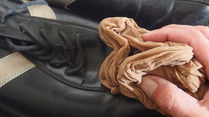 Eine Hand h&auml;lt kaputte Nylons und reinigt damit einen schwarzen Schuh, um ihn aufzufrischen und zu sparen.