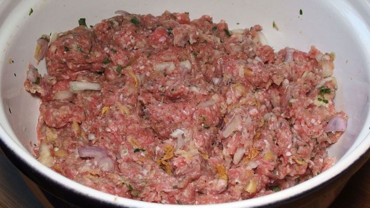 Eine Sch&uuml;ssel mit rohem Hackfleisch, vorbereitet f&uuml;r Bouletten, steht auf einem Tisch in einer heimischen K&uuml;che.