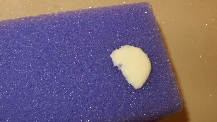 Eine kleine Menge Scheuermilch auf einem blauen Schwamm, bereit zum Reinigen einer glatten Oberfl&auml;che.