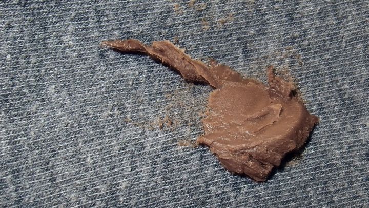 Ein Nutellafleck ist auf einem blauen Jeansstoff zu sehen, der sich schmutzig abhebt und leicht verwischt wirkt.