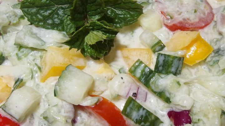 Bunte Salatst&uuml;cke aus Gurken, Tomaten und Mangos sind in einer cremigen So&szlig;e gemischt und mit einem Minzblatt garniert.