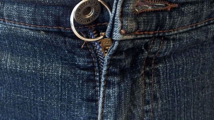 Ein Rei&szlig;verschluss an einer Jeans &ouml;ffnet sich, w&auml;hrend der Stoff blau und eng anliegend ist. Die Metallteile gl&auml;nzen.