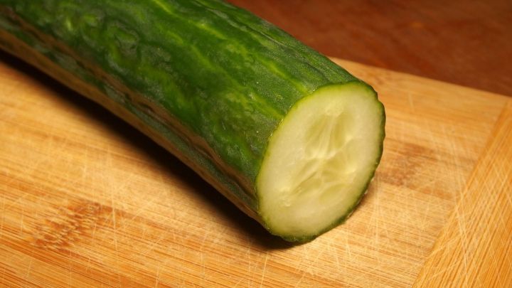 Eine frische Gurke liegt auf einem Holzbrett, schneidet sie in Scheiben, um sie als Geschmacksverst&auml;rker zu verwenden.