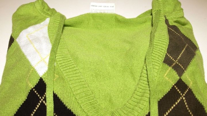 Ein grüner Pullover mit einem v-Ausschnitt liegt ordentlich auf einer Oberfläche. Das Pflegeetikett ist sichtbar.