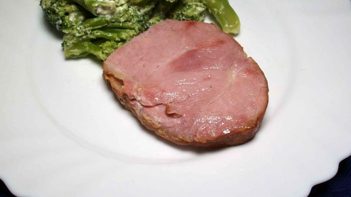 Ein saftiges St&uuml;ck Kasselerbraten liegt auf einem wei&szlig;en Teller, begleitet von gr&uuml;nen Beilagen in einem eleganten Ambiente.