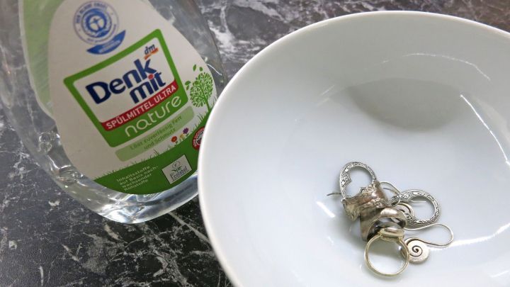 Ein Teller mit Schmuckst&uuml;cken liegt neben einer Flasche Sp&uuml;lmittel. Der Kontext zeigt eine Reinigungssituation.