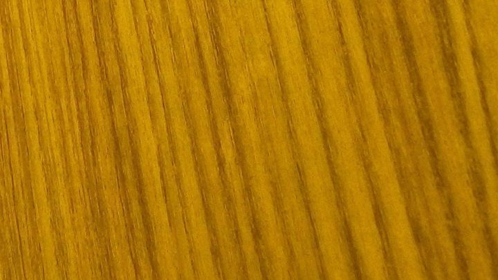 Eine Holzoberfl&auml;che mit einer gl&auml;nzenden, ockerfarbenen Patina zeigt die Wirkung von Lein&ouml;l, in einem hellen Umfeld.