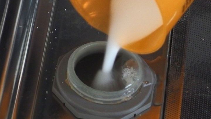 Ein orangefarbener Beh&auml;lter f&uuml;llt Sp&uuml;lmaschinensalz in den Salzbeh&auml;lter einer Sp&uuml;lmaschine, die gl&auml;nzend und sauber aussieht.