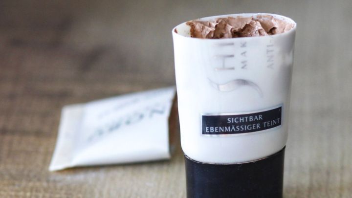 Ein Make-Up-Tube mit Resten steht auf einem Tisch, w&auml;hrend ein leeres Sachet daneben liegt.