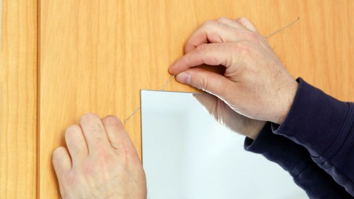 Zwei H&auml;nde ziehen an einem Faden, um ein St&uuml;ck Spiegelklebeband von einer Holzoberfl&auml;che zu entfernen.