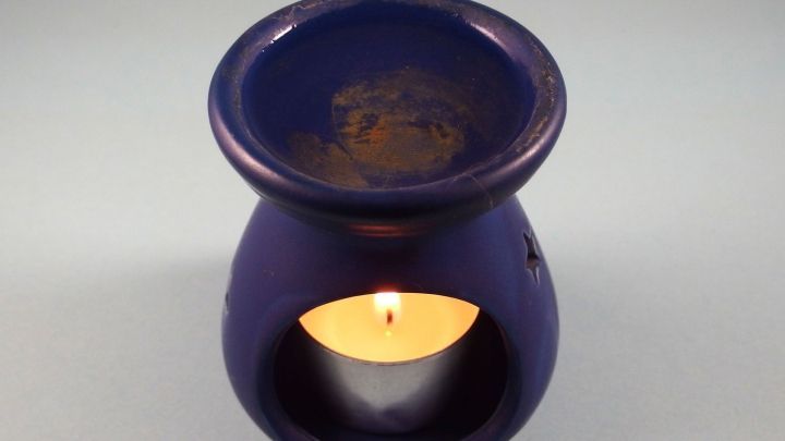 Ein lila Duft&ouml;l-Gef&auml;&szlig; steht auf einer glatten Oberfl&auml;che, w&auml;hrend eine Kerze im Inneren brennt und Aroma verbreitet.