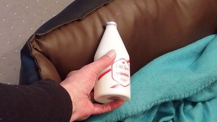 Ein Hand h&auml;lt eine Flasche Rasierwasser, die auf einer Ledercouch liegt, um einen Kugelschreiberfleck zu entfernen.
