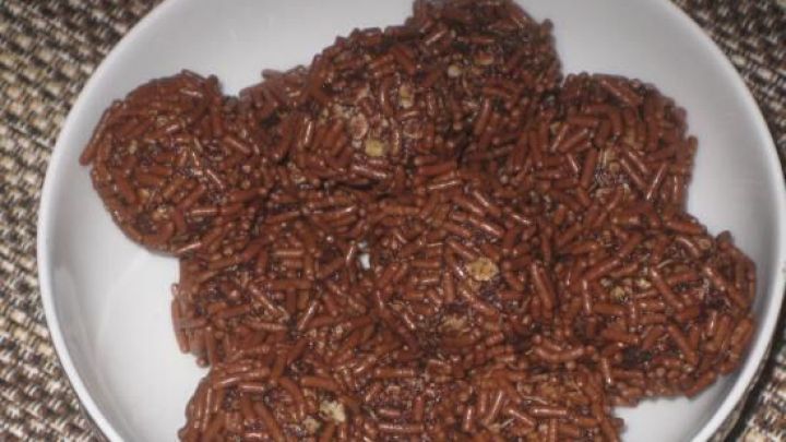 Rumkugeln liegen in einer weißen Schüssel, bedeckt mit Schokostreuseln, auf einem gemusterten Tischset.