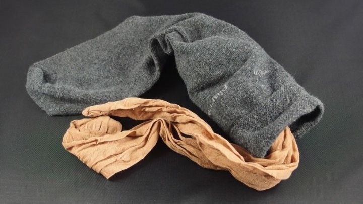 Schwarze Nylon-Str&uuml;mpfe und hautfarbene Strumpfhosen liegen &uuml;bereinander auf einem dunklen Hintergrund, bereit zum Waschen.