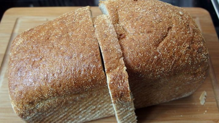 Ein frisch gebackenes Brot aus dem Brotbackautomaten liegt auf einem Holzbrett, w&auml;hrend es in Scheiben geschnitten wird.