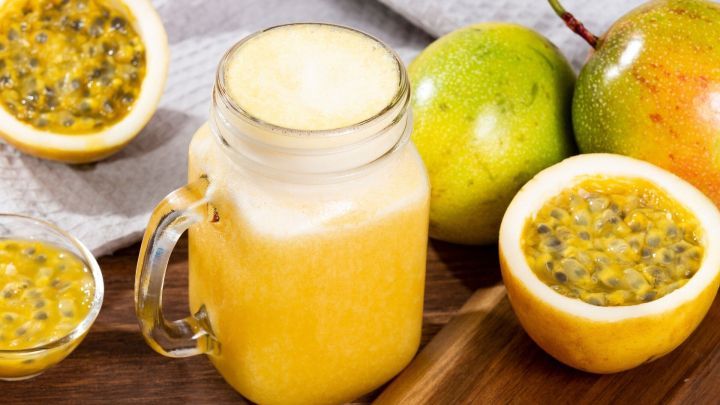 Ein Glas frischer Hahler Milch steht auf einem Tisch, umgeben von Passionsfr&uuml;chten und Fr&uuml;chten auf einem Holzbrett.