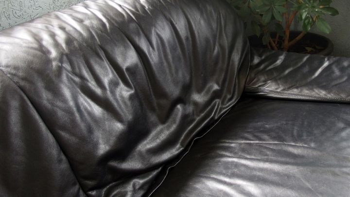 Ein schwarzes Ledersofa ruht in einer eleganten Umgebung, die Polsterung ist leicht zerknittert und gl&auml;nzend.