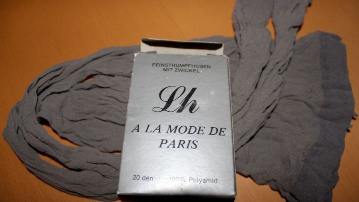 Feinstrumpfhosen liegen lose um eine offene Verpackung auf einem Tisch. Die Packung zeigt elegante Schriftz&uuml;ge.
