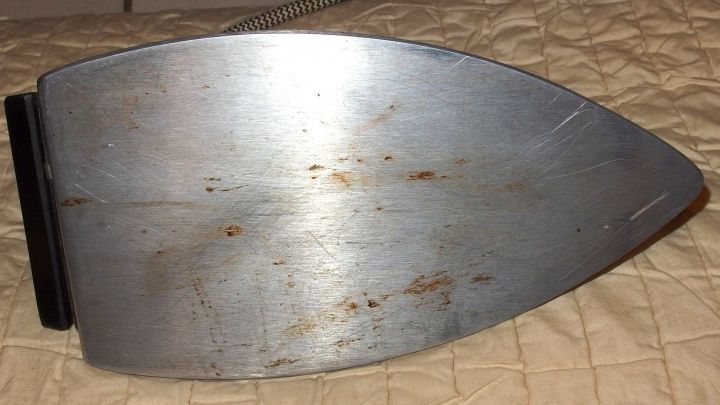 Eine gl&auml;nzende B&uuml;geleisenunterseite liegt auf einem hellen, strukturierten Untergrund, bereit f&uuml;r die Reinigung mit &Ouml;l und Rasierklinge.