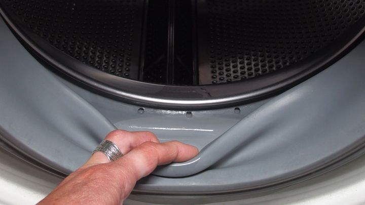 Ein Hand greift nach dem Gummi der Waschmaschine, der m&ouml;glicherweise schimmelig ist. Der Innenraum der Maschine ist sichtbar.