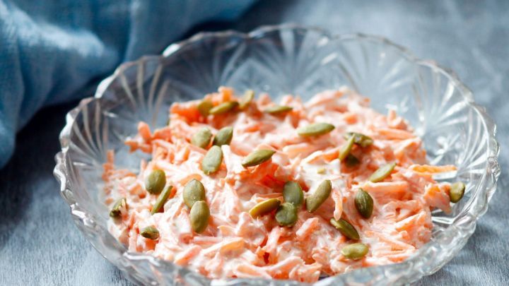 Ein frischer M&ouml;hrensalat mit K&uuml;rbiskernen liegt dekorativ in einer Kristallsch&uuml;ssel auf einem blauen Tuch.