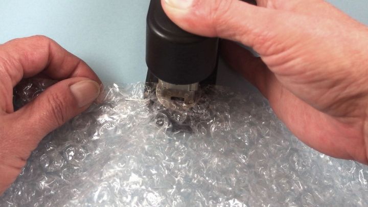 Eine Hand h&auml;lt einen Hei&szlig;luftf&ouml;n, der &uuml;ber Luftpolstertaschen gehalten wird, um diese wiederzuverwenden oder selbstzumachen.