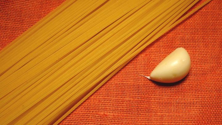 Lange Spaghetti liegen neben einer Zehe frischem Knoblauch auf einem roten Hintergrund, bereit f&uuml;r einen Salat.