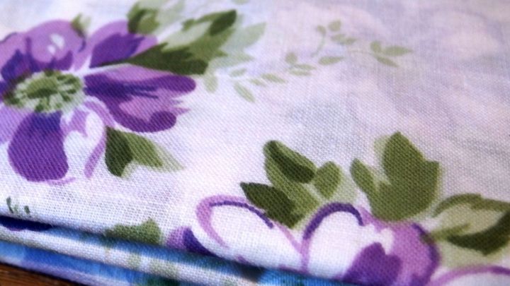 Ein bunte, floral gemusterte Serviette liegt gefaltet auf einem Tisch, bereit zum B&uuml;geln mit einem nassen Handtuch.