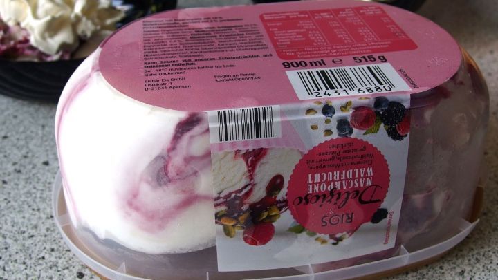 Eine Packung gefrorenes Dessert liegt auf einer K&uuml;chenarbeitsplatte, umgeben von Nebensachen wie Sahne und Beeren.