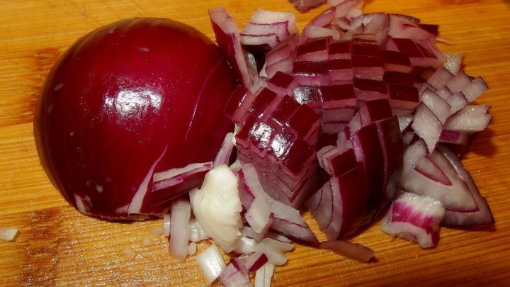 Eine Zwiebel steht auf einem Holzbrett, neben ihr liegen klein gehackte Zwiebelst&uuml;cke, die auf die Verwendung bei Erk&auml;ltung hinweisen.