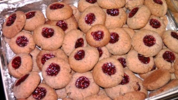 Pl&auml;tzchen mit Himbeermarmelade in der Mitte liegen dicht an dicht in einer silbernen Backform.