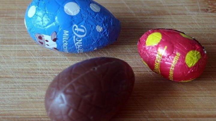 Bunte Schokoladeneier liegen auf einem Holzuntergrund, bereit zum Genie&szlig;en, vielleicht um Knoblauchgeruch zu mildern.